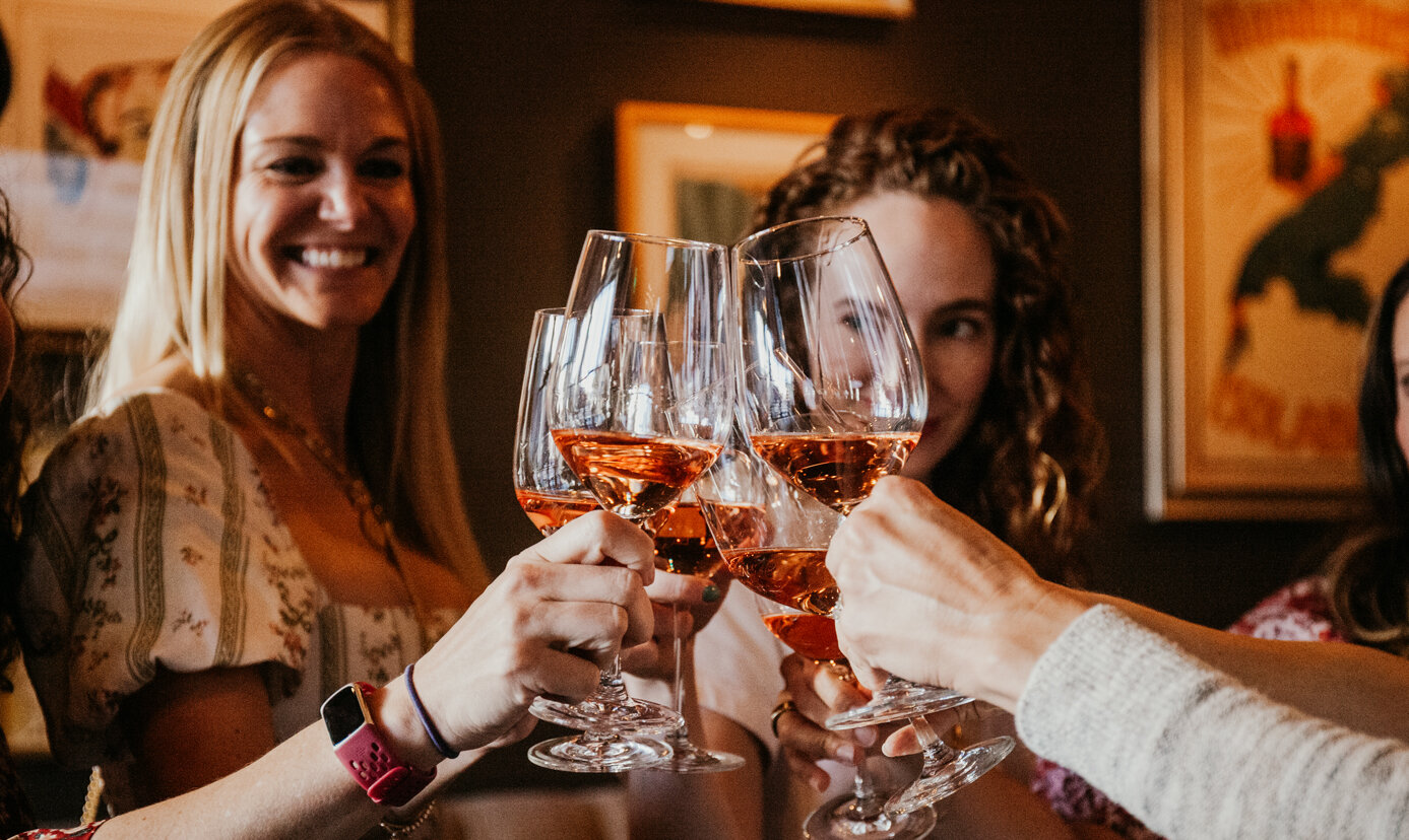 Image of women clinking wine glasses in a restaurant with moody lighting